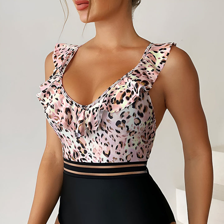 Dos d'une femme portant un maillot de bain une pièce à imprimé léopard rose et noir, avec des volants aux épaules et des bretelles croisées.