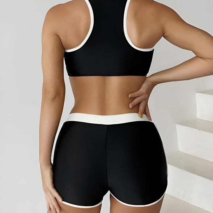 Femme portant un ensemble de sport deux pièces noir et jaune fluo, composé d'un haut avec fermeture éclair et d'un short, idéal pour l'entraînement ou la natation.