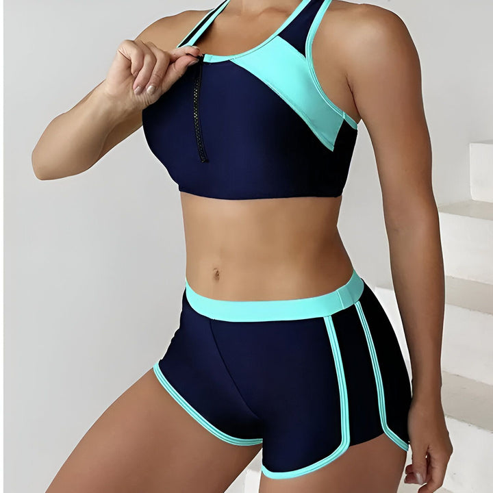 Gros plan d'une femme portant un maillot de bain deux pièces de sport noir et turquoise. Le haut est un soutien-gorge de sport zippé et le bas est un short de bain.