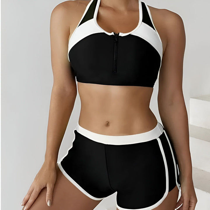 Image d'une femme portant un maillot de bain deux pièces bleu marine et turquoise. Le haut est un soutien-gorge de sport à fermeture éclair et le bas, un short de bain.