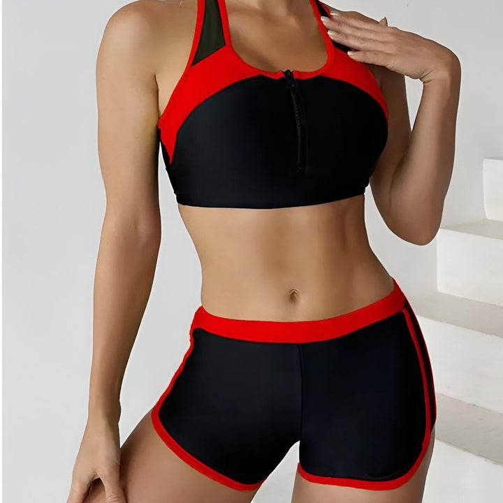 Femme en maillot de bain deux pièces noir et rouge. Haut de sport avec fermeture éclair, short de bain bordé de rouge. Vêtements de plage modernes et confortables.
