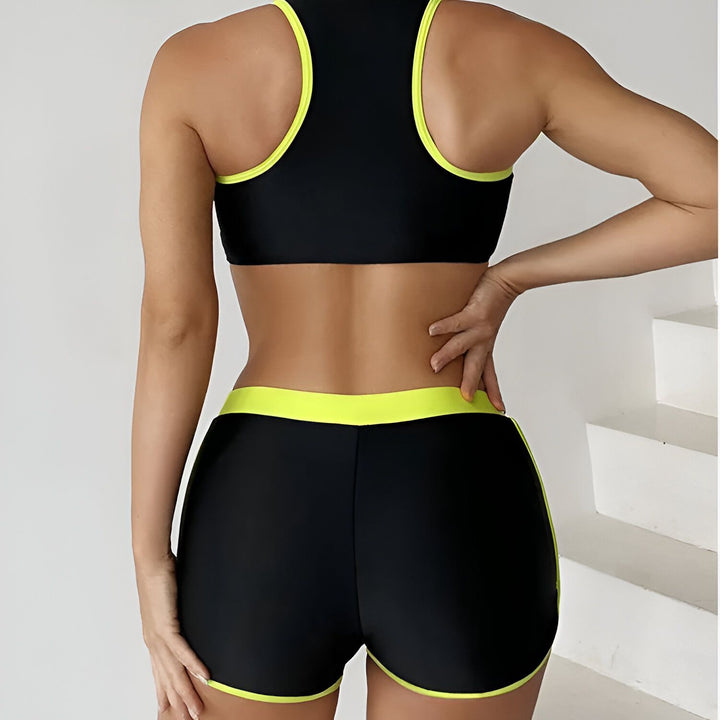 Femme portant un maillot de bain deux pièces bleu marine et bleu turquoise. Haut de sport avec fermeture éclair et short de bain assorti. Tenue de plage tendance et confortable.