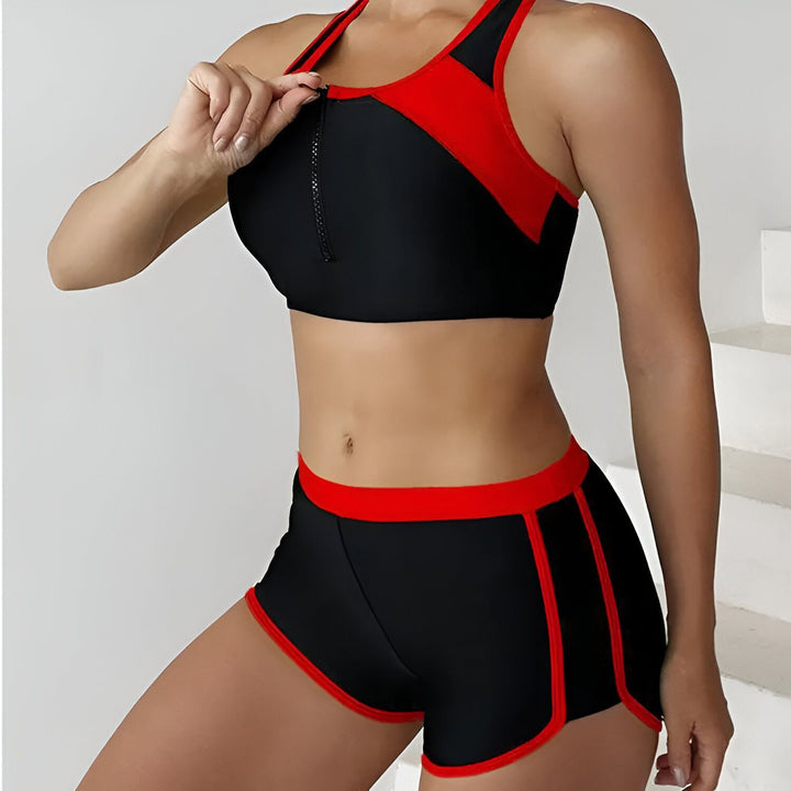 Femme portant un ensemble de sport deux pièces noir et rouge. Haut de sport avec fermeture éclair devant et short court.