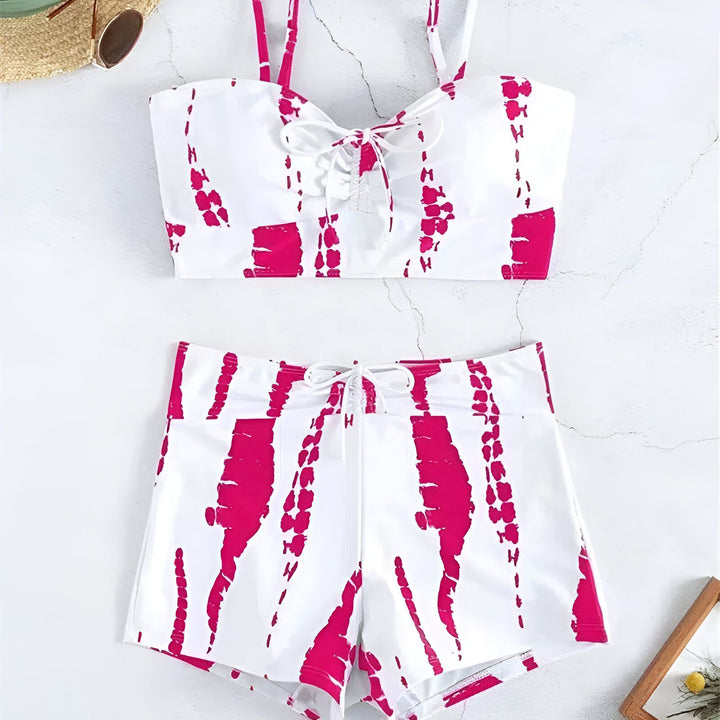 Jeune femme blonde en maillot de bain deux pièces rose et blanc posant près d'une piscine par une journée ensoleillée. Cheveux longs blonds, peau claire, look de plage.