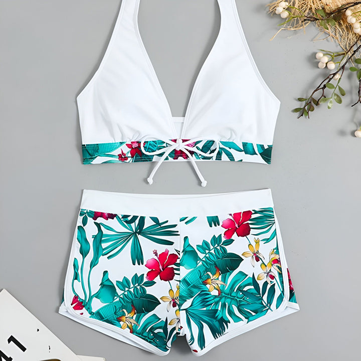 Ensemble de maillot de bain deux pièces blanc à imprimé tropical, comprenant un haut de bikini à col en V et un short de bain à taille haute. Idéal pour la plage ou la piscine.