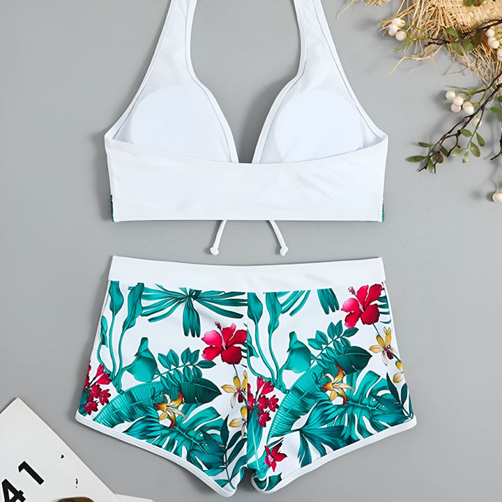Gros plan d'une femme portant un maillot de bain deux pièces blanc avec un motif floral tropical vert et rouge. Le haut est un soutien-gorge avec des liens et le bas est un short taille haute. Idéal pour l'été et la plage.