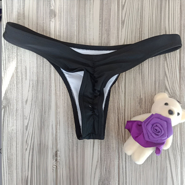 Culotte de bikini rouge sur un fond en bois rustique, avec un carton de célébration à côté. Style effronté et coupe basse, parfait pour l'été.