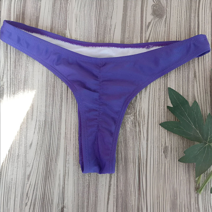 Image d'un bas de bikini vert fluo sur un fond en bois clair, avec une carte rose à motifs de cactus. Le bikini est simple et moderne, parfait pour l'été.