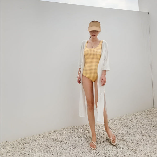 Une femme portant un maillot de bain jaune à carreaux et une visière de paille, vue de dos. Idéal pour la plage ou la piscine, look tendance et estival.