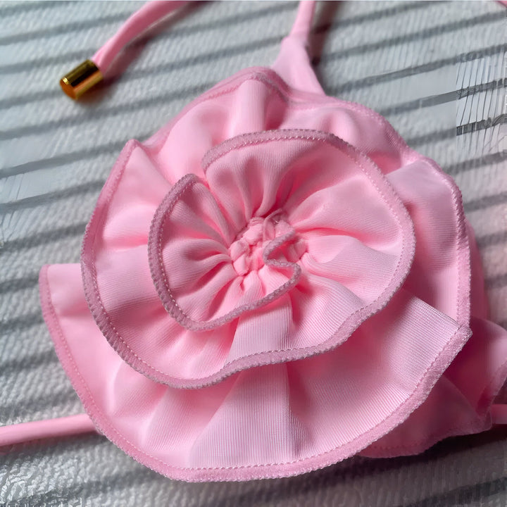 Femme en bikini rose avec motifs floraux, posant devant un mur de pierre texturé. Mode estivale, maillot de bain tendance.