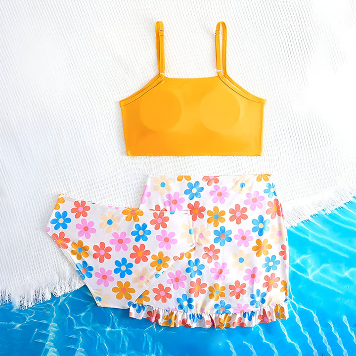 Vue aérienne d'un ensemble de maillot de bain deux pièces jaune et fleuri, complété par un chapeau de paille, des lunettes de soleil roses et une étoile de mer sur un fond bleu aquatique. Idéal pour la mode estivale, les vacances à la plage et la présentation de vêtements.