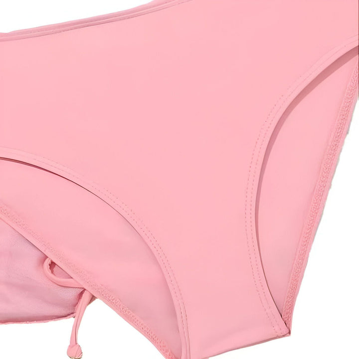 Gros plan d'un bas de bikini rose clair, mettant en valeur la couture et les détails des cordons latéraux. Idéal pour la mode estivale ou la lingerie.