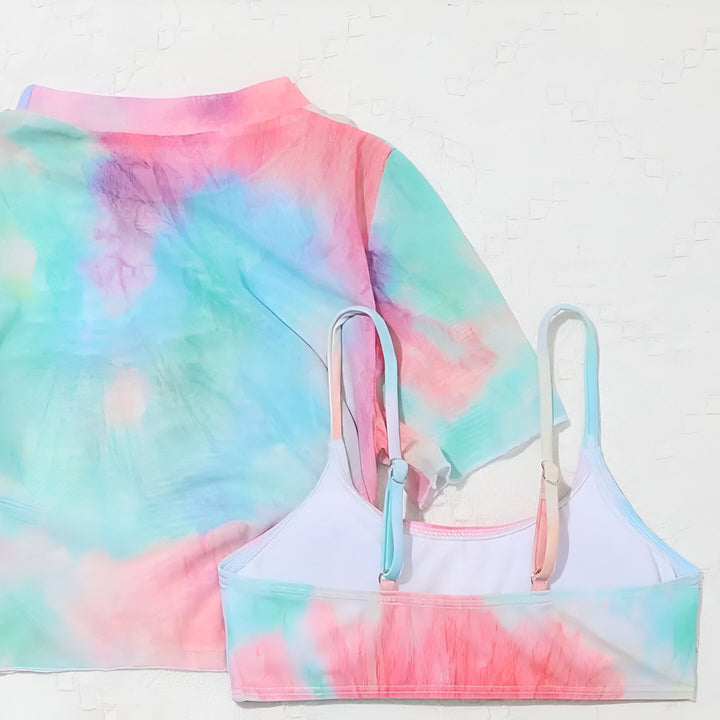 Ensemble de bikini tie-dye pastel pour femmes avec haut à manches courtes, haut de bikini, jupe et bas de bikini, chapeau de paille en arrière-plan.