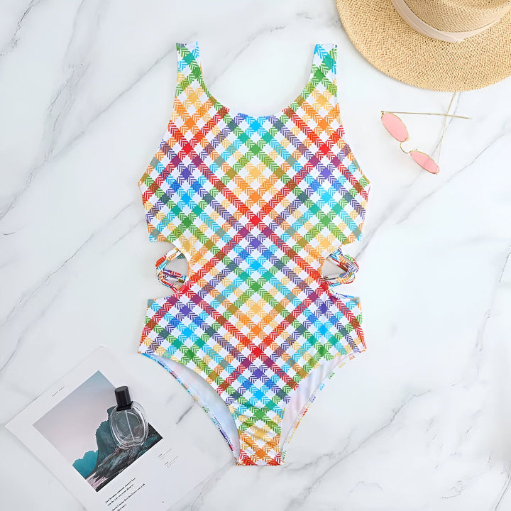 Maillot de bain une pièce multicolore à carreaux avec découpes sur les côtés, posé sur fond marbré blanc. Vêtement de plage tendance pour femme, style estival.
