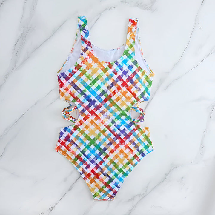 Maillot de bain une pièce à carreaux multicolores, coupé sur les côtés, avec chapeau de paille, lunettes de soleil et magazine sur fond marbré. Idée cadeau, mode été.