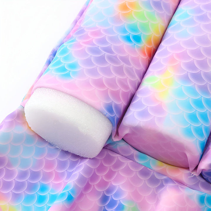 Gros plan d'un maillot de bain pour enfant avec un motif d'écailles de sirène multicolores, comprenant un nœud décoratif et des flotteurs intégrés pour la sécurité dans l'eau.