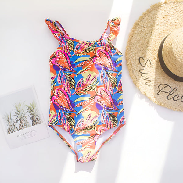 Image rapprochée d'un maillot de bain une pièce à imprimé floral coloré, avec un bord volanté et un chapeau de paille en partie visible, évoquant l'été et les vacances.