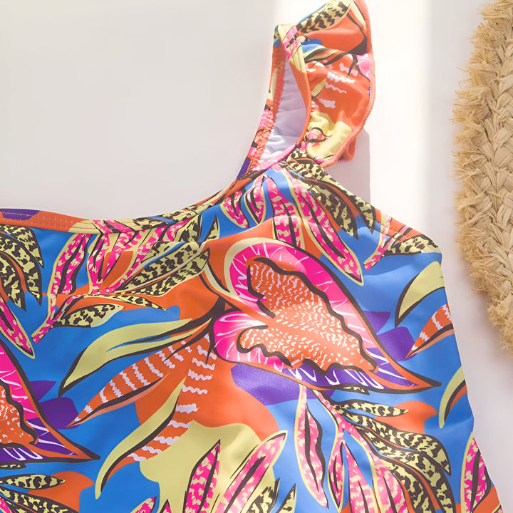 Maillot de bain une pièce coloré à motifs tropicaux, chapeau de paille avec inscription "Sun Please" et carte postale avec ananas sur fond blanc. Idéal pour l'été et les vacances.