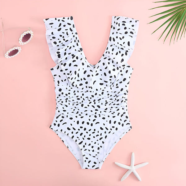 Maillot de bain une pièce blanc à pois noirs et à volants sur fond rose. Idéal pour la plage ou la piscine. Style estival et tendance.