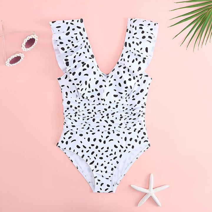 Maillot de bain une pièce blanc à pois noirs et à volants sur fond rose. Idéal pour la plage ou la piscine. Style estival et tendance.