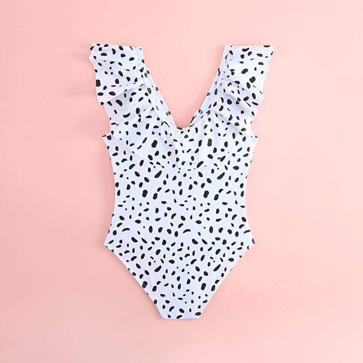 Maillot de bain une pièce blanc à pois noirs avec volants, sur fond rose avec lunettes de soleil originales, étoile de mer et feuille de palmier. Vêtements d'été, mode plage.