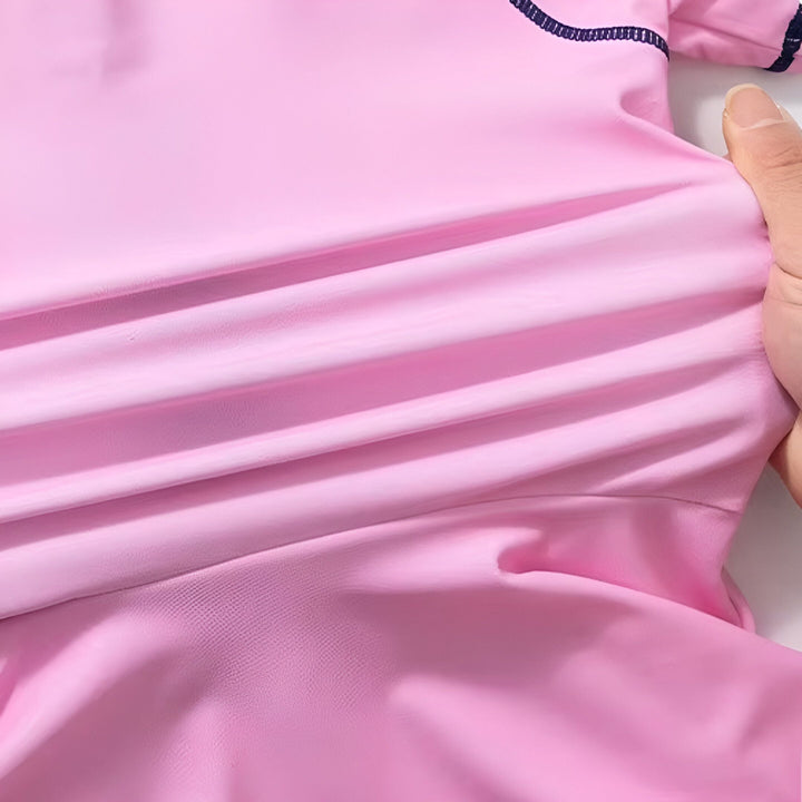 Maillot de bain rose pour fille avec l'image d'Elsa de La Reine des Neiges, manches courtes et jupe, fermeture éclair sur le devant et détails bleu marine.