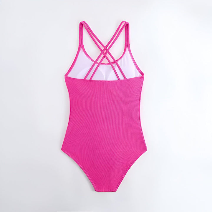 Maillot de bain rose vif une pièce pour fille, avec bretelles croisées. À côté, se trouve un sac à dos vert en forme de triangle, une étoile de mer rose et une feuille de palmier. Idéal pour les vacances d'été à la plage.