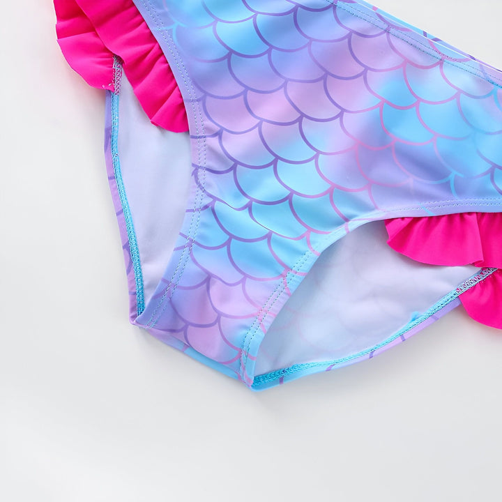 Haut de maillot de bain pour enfant, motif écailles de sirène bleu et violet, avec une bretelle rose agrémentée d'un nœud rose. Idéal pour la plage et la piscine.