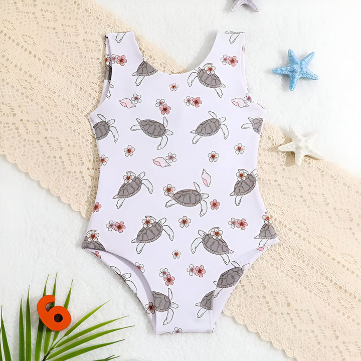 Maillot de bain une pièce pour enfant, imprimé de tortues et de fleurs sur fond blanc, idéal pour la plage ou la piscine. Design mignon et tendance pour les petites filles.