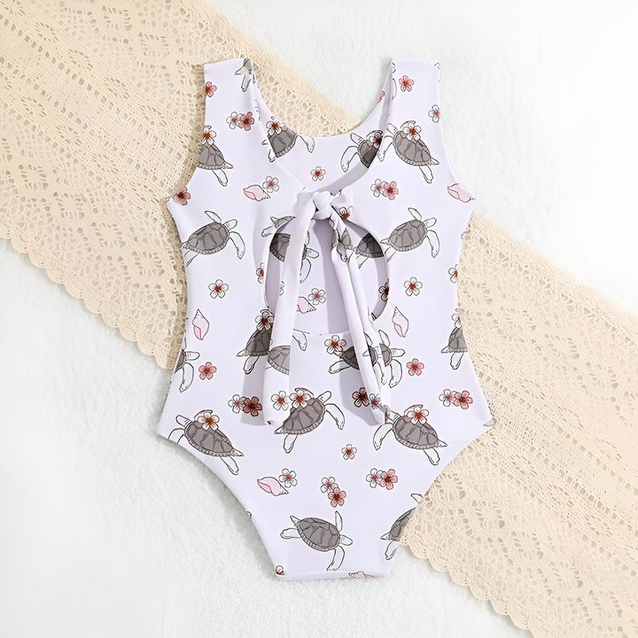 Maillot de bain blanc une pièce pour enfant avec motif tortues et fleurs, idéal pour la plage et la piscine.