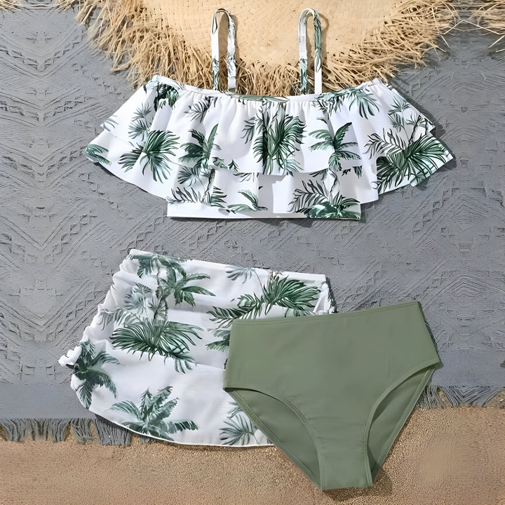 Ensemble de maillot de bain deux pièces pour femme. Haut à volants blanc avec motif de palmiers verts et fines bretelles. Bas de style jupe assorti avec un slip vert uni. Chapeau de paille en arrière-plan. Idéal pour la plage ou la piscine.