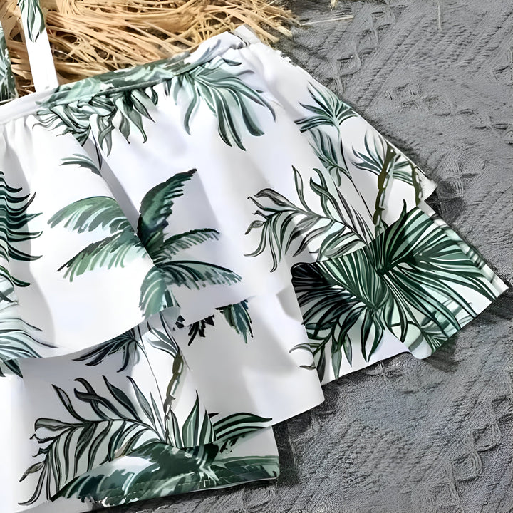 Gros plan sur un haut de bikini à volants blancs avec un motif de feuilles de palmier vertes luxuriantes. Idéal pour la plage, la piscine et les vacances tropicales.