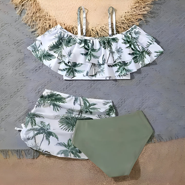 Ensemble de maillot de bain deux pièces pour femme avec imprimé tropical blanc et vert, comprenant un haut à volants et une culotte de bain taille haute de couleur unie, présenté avec un chapeau de paille.