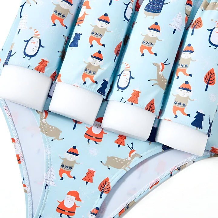 Maillot de bain bleu clair avec motifs de Noël: Père Noël, pingouins, rennes, bonhommes et sapins de Noël. Bretelles blanches. Idéal pour les fêtes à la piscine en hiver.
