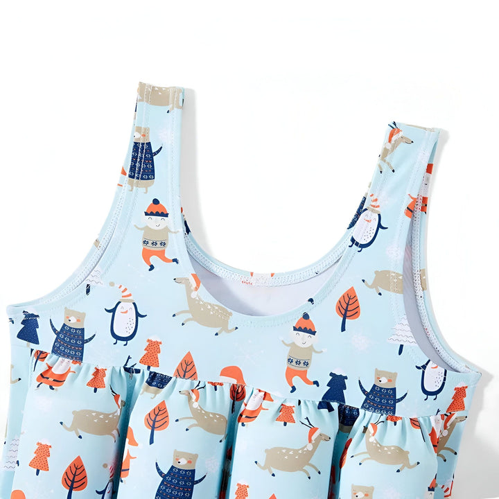 Détail d'un maillot de bain avec un motif festif d'hiver. On y voit des pères Noël, des ours, des pingouins, des rennes et des sapins sur un fond bleu clair. Idéal pour les fêtes de fin d'année.