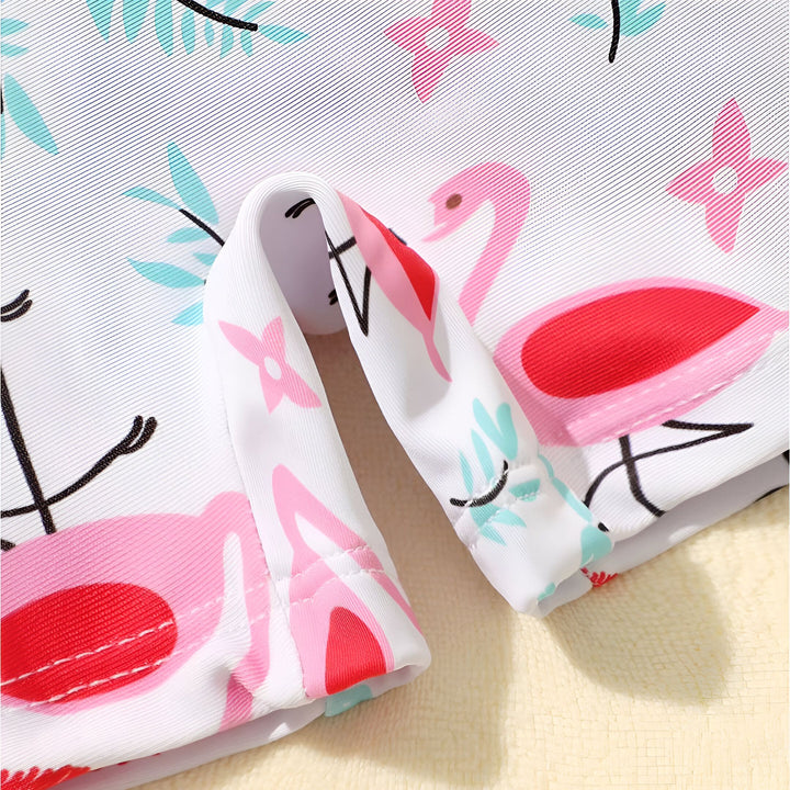 Gros plan sur le tissu d'un maillot de bain pour enfant avec des motifs de flamants roses, des fleurs roses et des feuilles turquoise.