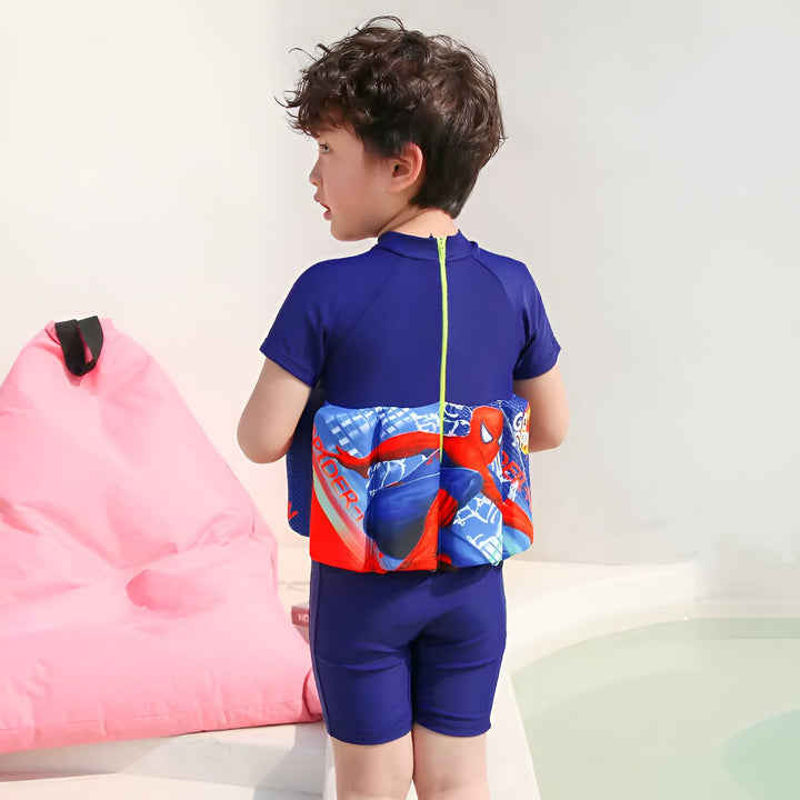Un garçon porte un maillot de bain bleu avec un motif Spiderman et un gilet de flottaison rouge et bleu avec Spiderman.