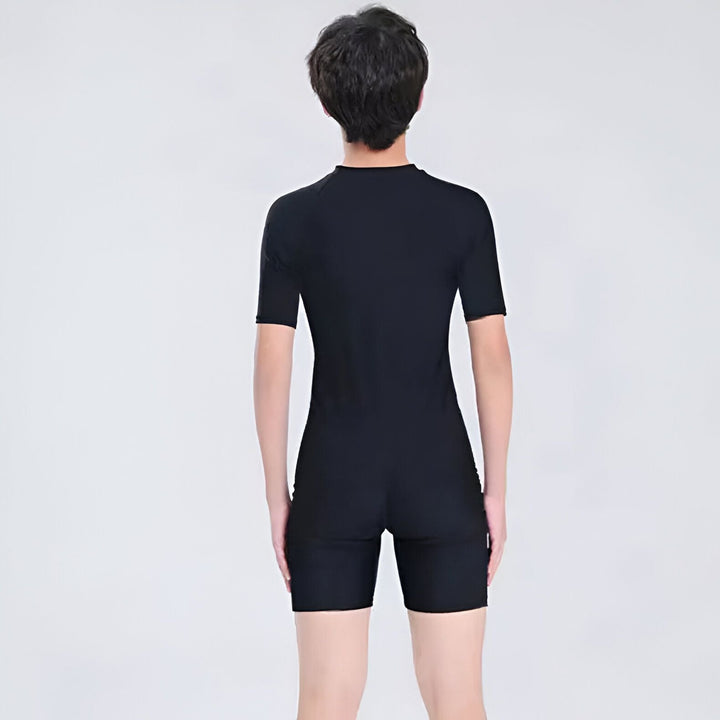 Jeune garçon souriant portant un maillot de bain une pièce noir et bleu avec fermeture éclair. Combinaison de natation à manches courtes pour enfant. Vêtement de sport aquatique unisexe pour la plage et la piscine.