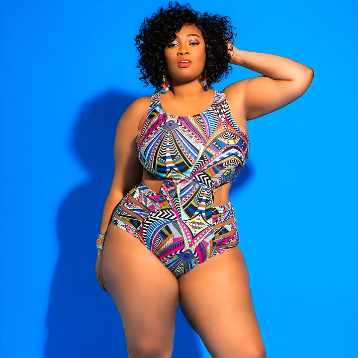 Une femme afro-américaine portant un maillot de bain coloré avec découpes, des lunettes de soleil blanches et de grandes boucles d'oreilles dorées. Elle pose devant un fond bleu vif.