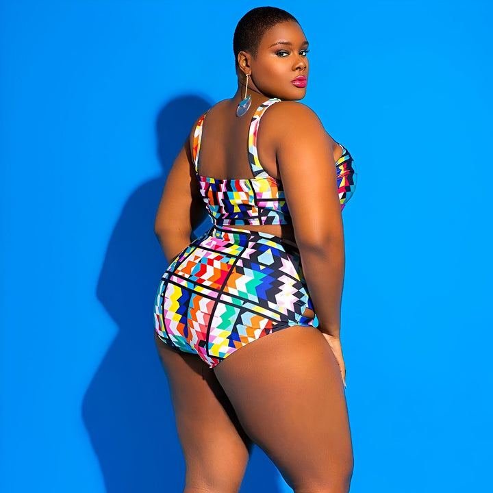 Femme noire posant en maillot de bain deux pièces grande taille à motifs géométriques colorés sur fond bleu. Elle a les cheveux bouclés et porte des bijoux dorés.