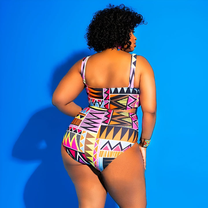 Femme vue de dos, portant un maillot de bain deux pièces coloré à motifs géométriques, bracelet assorti. Cheveux bouclés noirs et peau foncée. Fond bleu uni. Mode été, plage.