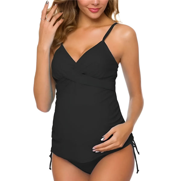 Femme enceinte souriante portant un maillot de bain tankini à pois bleu marine et blancs, les mains sur son ventre. Maillot de bain de maternité tendance et confortable. Mode future maman.