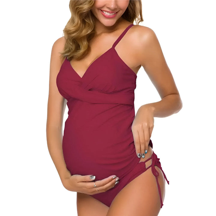 Femme enceinte souriante en maillot de bain tankini bleu marine, avec des bretelles fines et des cordons de serrage sur le côté. Idéal pour la natation et la détente à la plage.