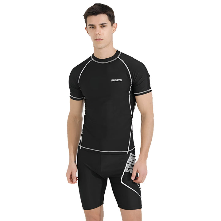 Homme de dos portant un rashguard noir à manches courtes et un short de bain assorti avec des détails blancs. Vêtements de sport pour activités aquatiques, protection solaire.