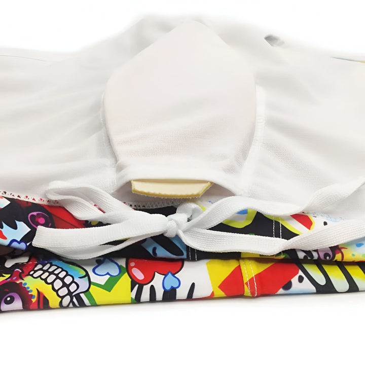 Homme torse nu en slip de bain imprimé graffiti, accompagné d'une protection pénienne en mousse, sur fond blanc.