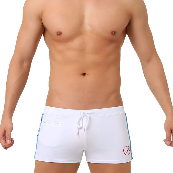 Homme torse nu en slip de bain noir avec cordon blanc et bande bleue sur fond blanc. Idéal pour la natation ou la plage. Mode masculine estivale.