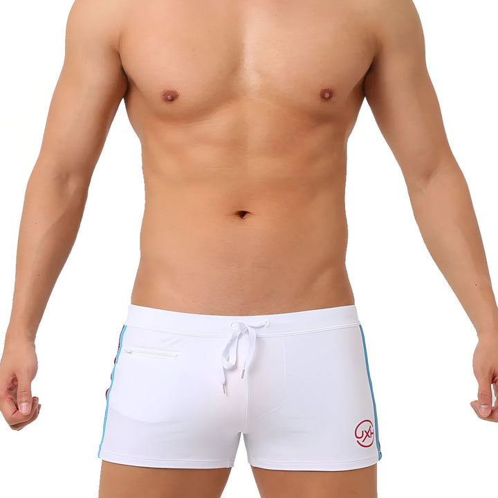 Homme torse nu en slip de bain noir avec cordon blanc et bande bleue sur fond blanc. Idéal pour la natation ou la plage. Mode masculine estivale.