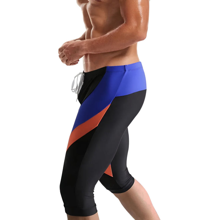 Image d'un maillot de bain homme orange, noir et jaune, coupé au niveau du genou, avec un cordon blanc à la taille. Il est présenté sur un fond blanc.