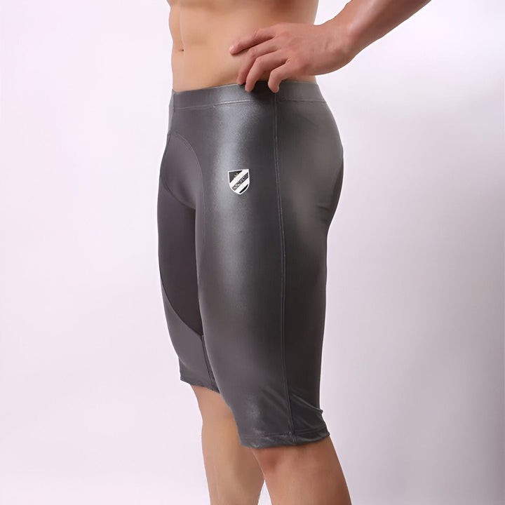 Pantalon de sport gris argenté, coupe 3/4. Empiècements unis, logo écusson sur la jambe. Vêtement de fitness moderne.