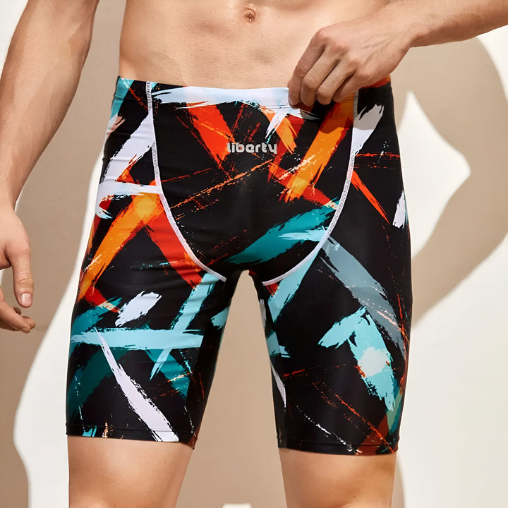 Homme torse nu portant un maillot de bain noir à motifs multicolores, idéal pour la natation ou la plage.